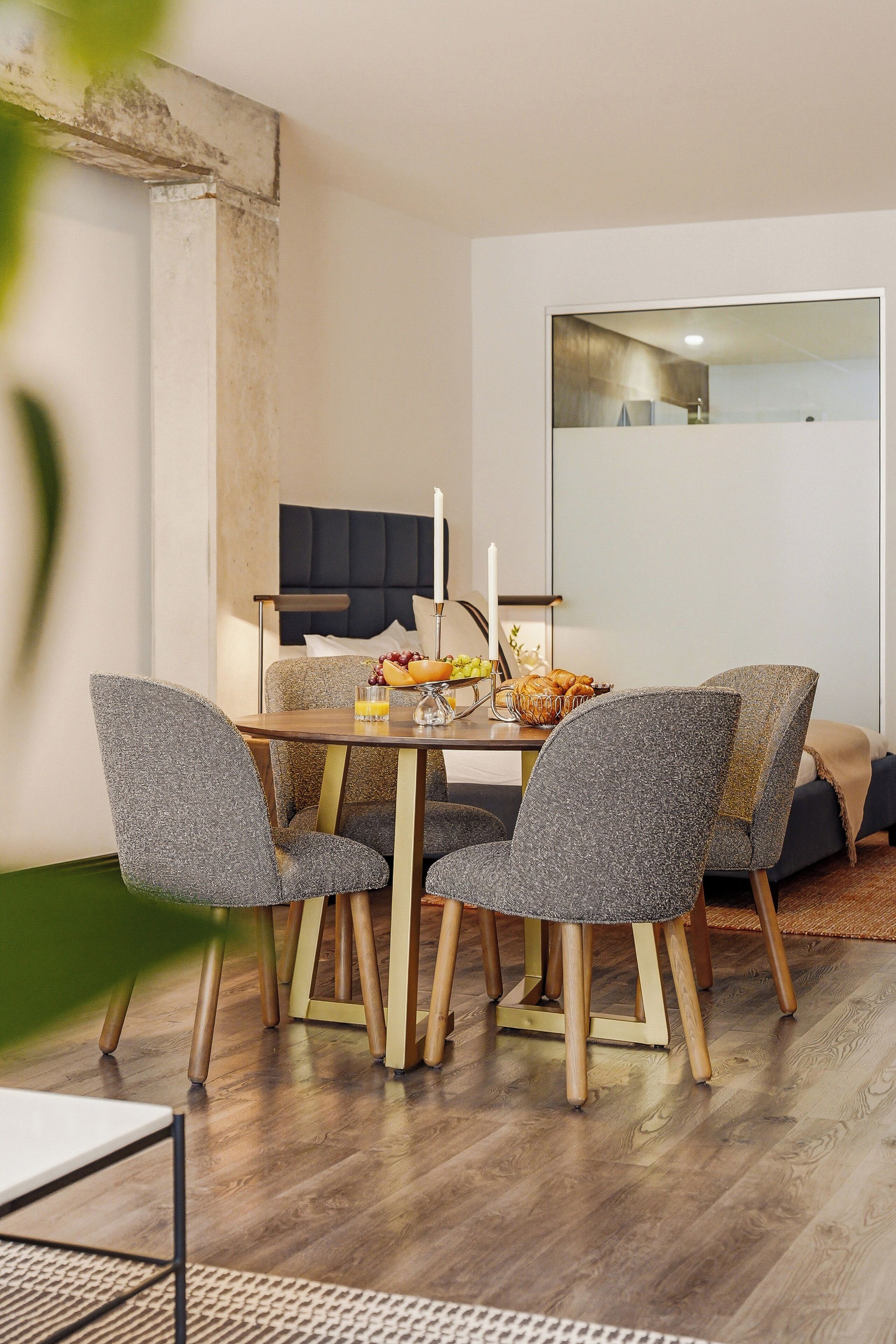 Un coin repas avec une table dressée pour quatre personnes, des chaises, une bougie et un panier de fruits.