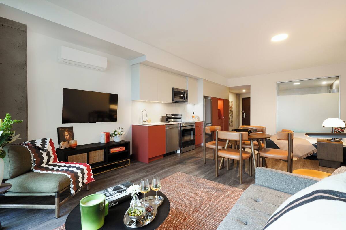 A modern living room with a sofa, a coffee table, a TV, and a kitchen area with a microwave and oven.