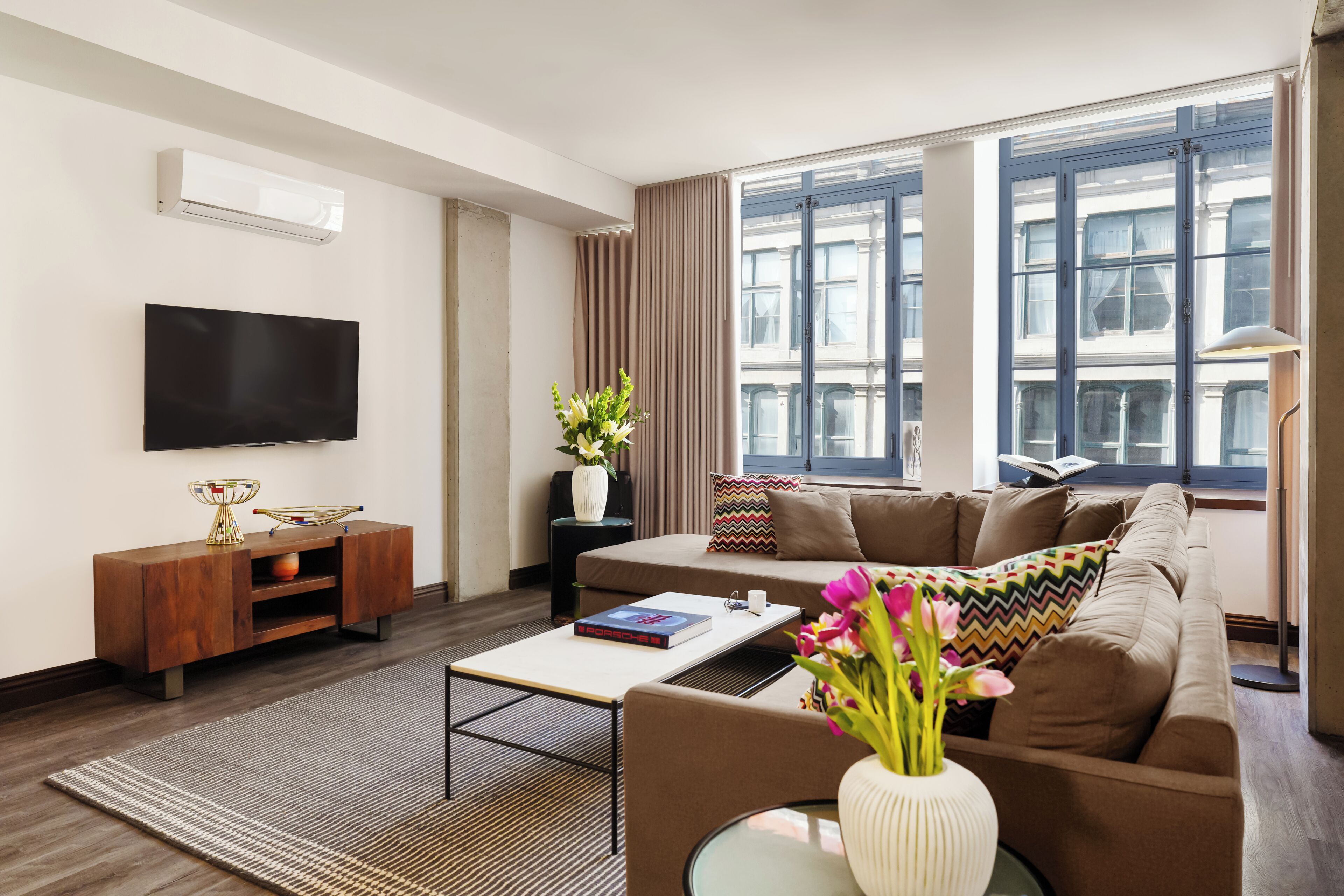 A modern living room with a flat-screen TV, a sofa, a coffee table, and a large window with curtains.