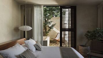 A bedroom with a bed, a nightstand, a lamp, a window with curtains, and a view of the outdoors.