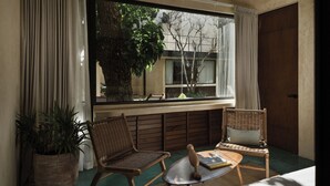 Een kamer met een groot raam, rieten meubels, een klein tafeltje en een potplant.