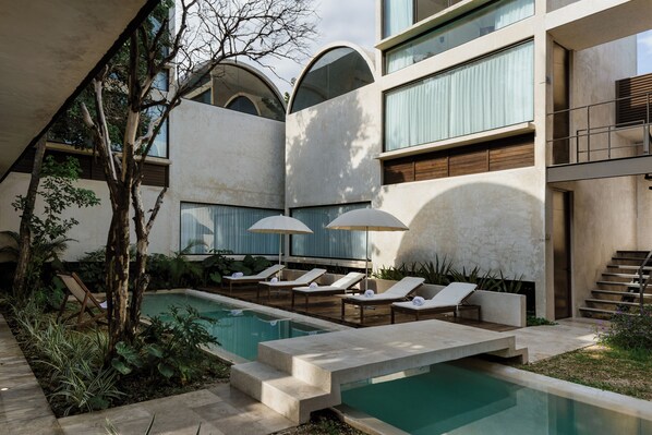 Un área de piscina moderna con sillones de descanso y sombrillas, rodeada de un diseño arquitectónico minimalista.