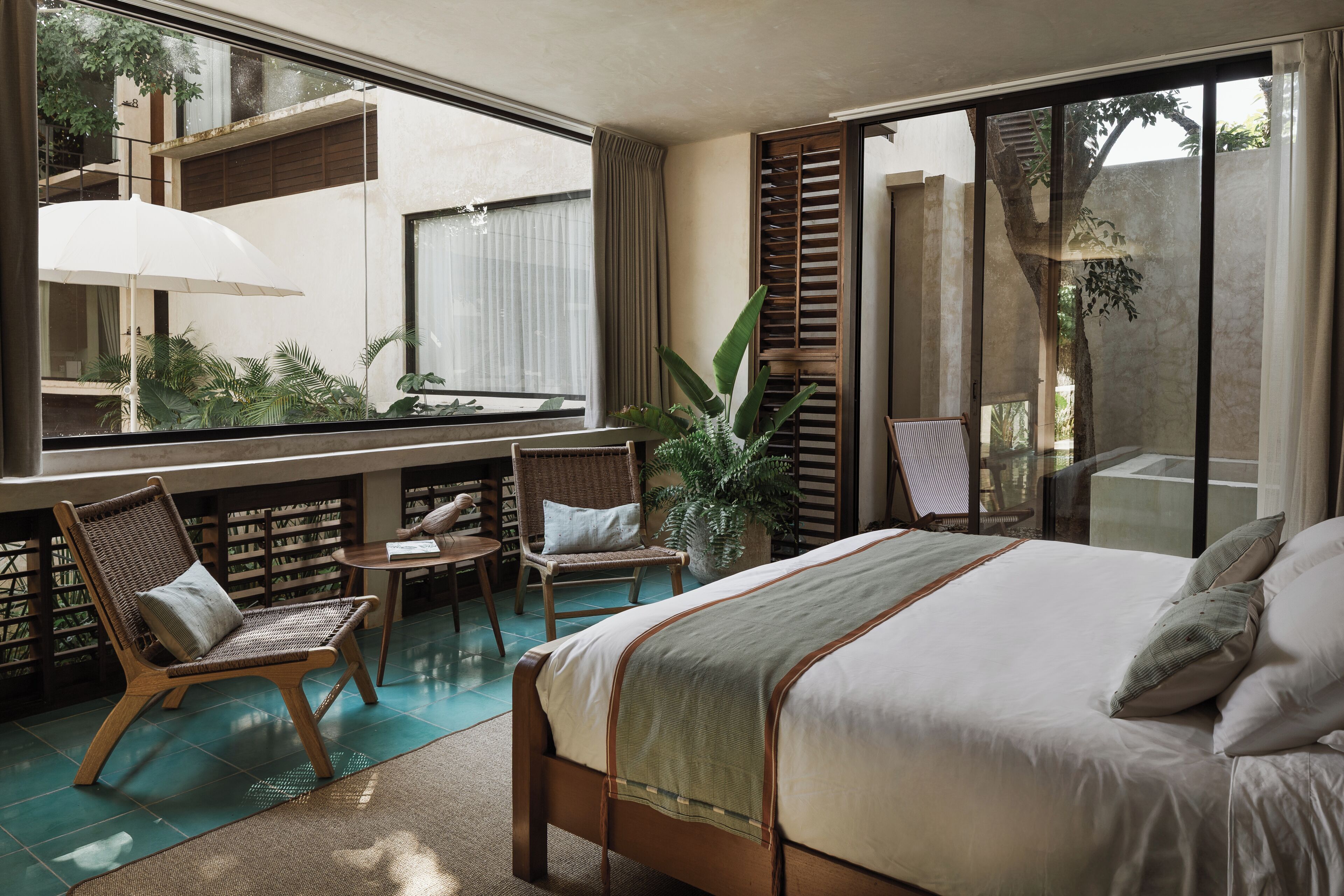 A bedroom with a large bed, a sitting area with chairs, a small table, and a large window overlooking a garden.