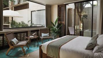 A bedroom with a large bed, a sitting area with chairs, a small table, and a large window overlooking a garden.