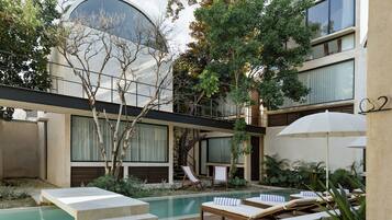 A modern building with a pool, lounge chairs, and a staircase leading to an upper level.