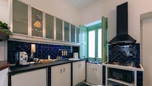 A modern kitchen with a built-in stove, a coffee machine, and a window with green curtains. - Elegant Apartment for 4 in Chiaia - Capri View Terrace (Napoli)