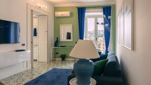 A living room with a TV, sofa, lamp, and a view of the city through the window. - Elegant Apartment for 4 in Chiaia - Capri View Terrace (Napoli)