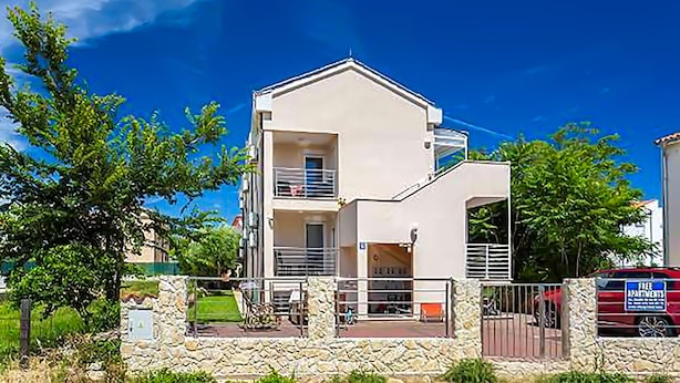 A modern two-story building with a balcony, a stone wall in front, and a red vehicle in the background. - 2 bedroom cozy apartment in Medulin (Medulin)