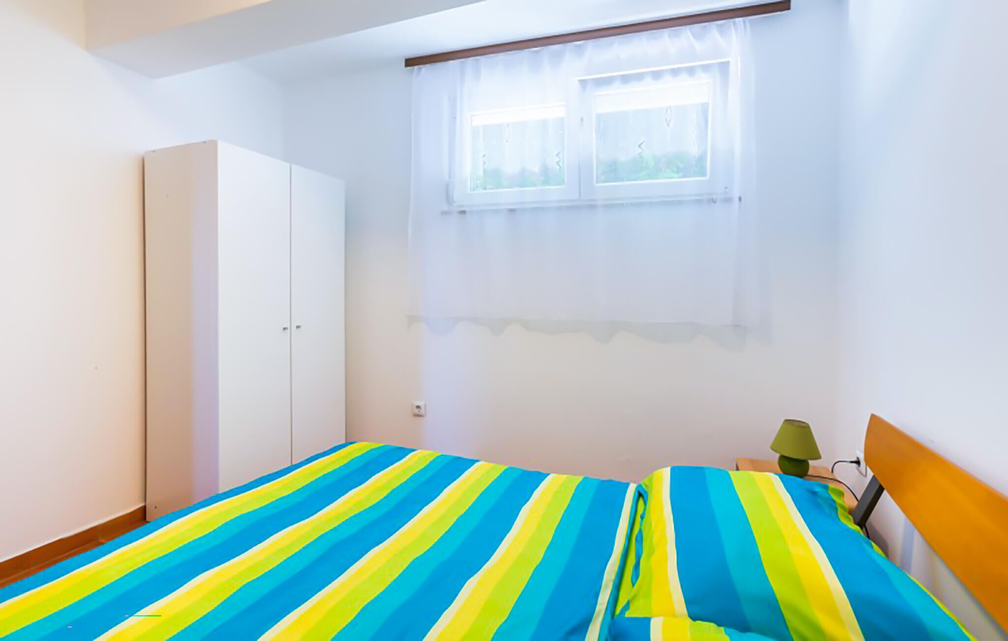 Quarto com duas camas, um guarda-roupa, uma janela com cortinas e uma mesa de cabeceira com abajur.