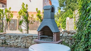 An outdoor stone oven with a table in front, surrounded by a stone wall and greenery. - 2 bedroom cozy apartment in Medulin (Medulin)