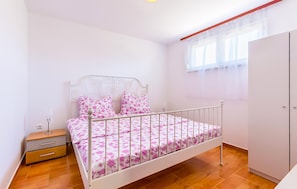 Ein Schlafzimmer mit einem Einzelbett, einem Nachttisch, einem Kleiderschrank und einem Fenster mit leichtem Vorhang.