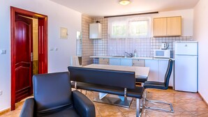 A compact kitchen with a dining area, a microwave, a refrigerator, and a red door. - 2 bedroom cozy apartment in Medulin (Medulin)