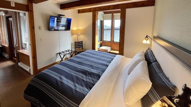 A hotel room with a bed, a television, a desk, a chair, and a window with a view. - Seaside Ucluelet Hotel (Ucluelet)