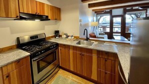 A modern kitchen with wooden cabinets, a stainless steel stove, a sink, and a window overlooking a deck. - Seaside Ucluelet Hotel (Ucluelet)