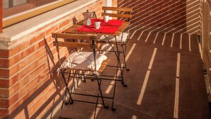 Ein Balkon mit Tisch und Stühlen, ein Fenster mit Jalousien und eine Backsteinmauer.
