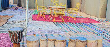 A rooftop with a patterned carpet, a metal table with chairs, and a row of drums.