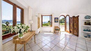 A room with a view of the sea, a wooden table with a vase of flowers, a chair, and a shelf with decorative items. - Villa Grotta Leone (Campania)