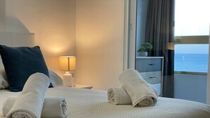 Un lit bien fait, avec des serviettes pliées, une lampe de chevet et une vue sur la mer par la fenêtre.