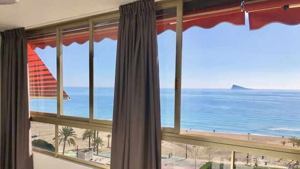 Une chambre dotée de grandes fenêtres donnant sur une plage, d’un balcon avec une balustrade et d’une vue sur la mer.