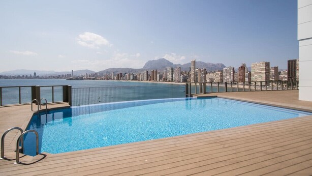 A rooftop pool with a city skyline and mountains in the background.