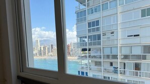 A multi-story building with balconies, a view of the sea, and other high-rise buildings in the background.