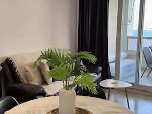 Una sala de estar con un sofá, una mesita, una planta en maceta y vistas al exterior a través de un ventanal grande.