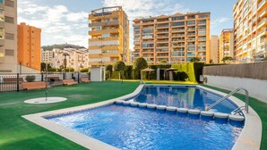 A swimming pool with a green lawn area, surrounded by multi-story buildings. - Apto 4 pax  a 2 minutos playa.A/C,terraza.Piscina. (La Vila Joiosa)