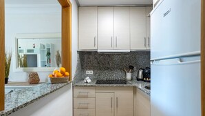 A kitchen with granite countertops, wooden cabinets, a refrigerator, and a window with a view of a room with plants and a shelf. - Apto 4 pax  a 2 minutos playa.A/C,terraza.Piscina. (La Vila Joiosa)