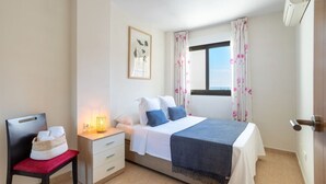 A bedroom with a bed, bedside table, chair, and a window with curtains. - Apto 4 pax  a 2 minutos playa.A/C,terraza.Piscina. (La Vila Joiosa)