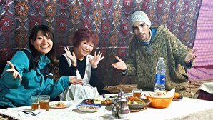 A dining area with a table set for a meal, surrounded by woven chairs. - Campsite. Where you are you going to spend your nights in desert. (Merzouga)