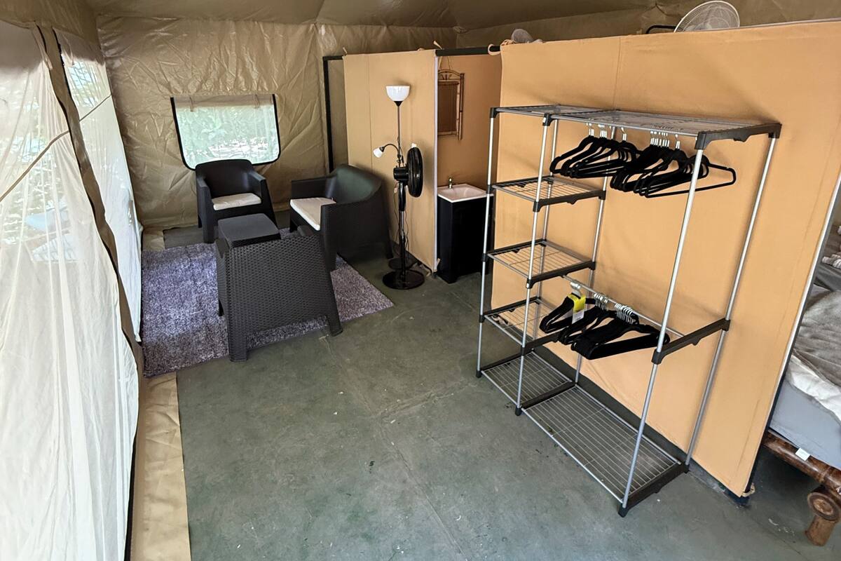 A tent with a bunk bed, a chair, a desk, a lamp, and a fan.