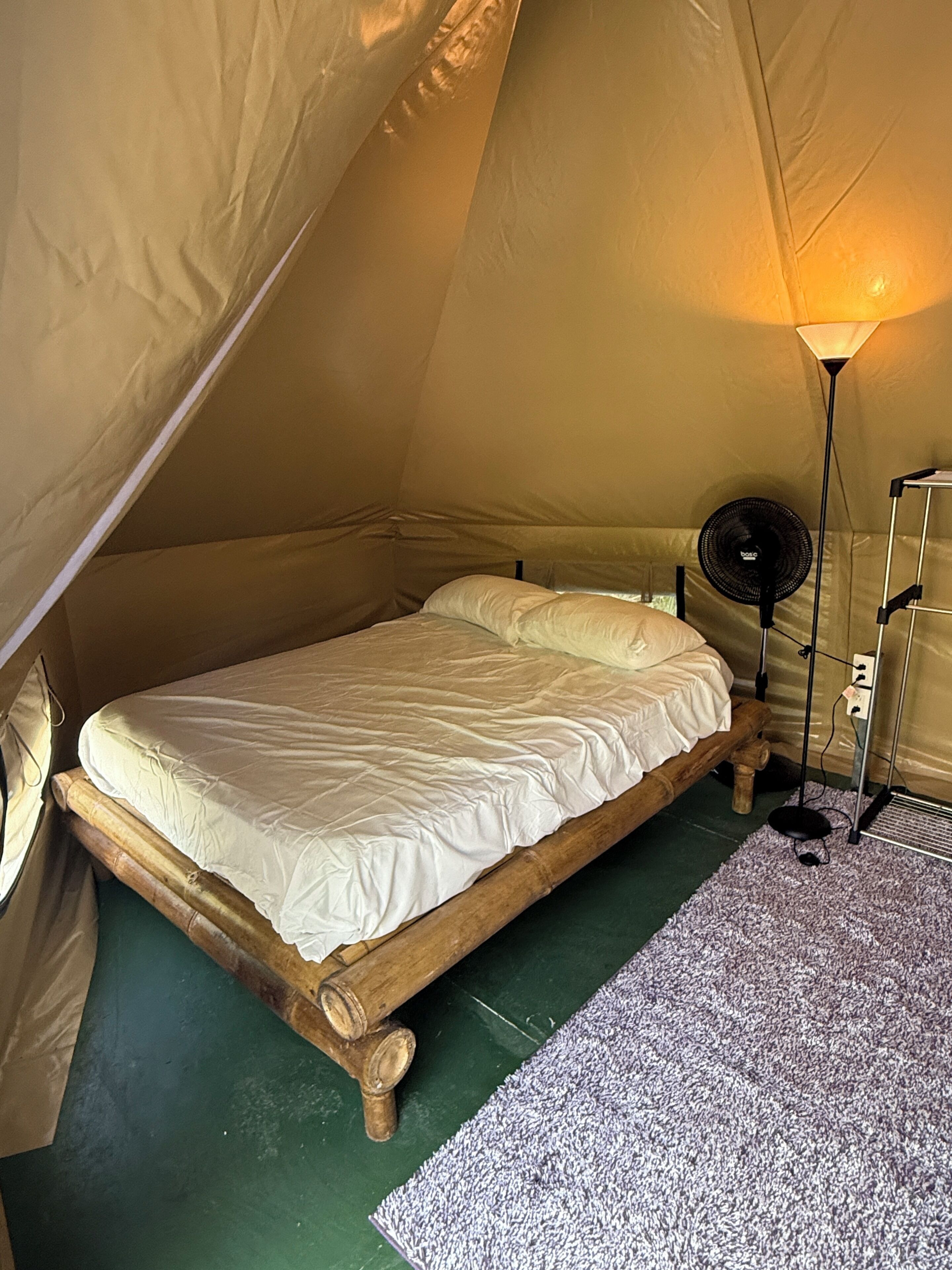 A tent with a bed, a floor lamp, and a power outlet.
