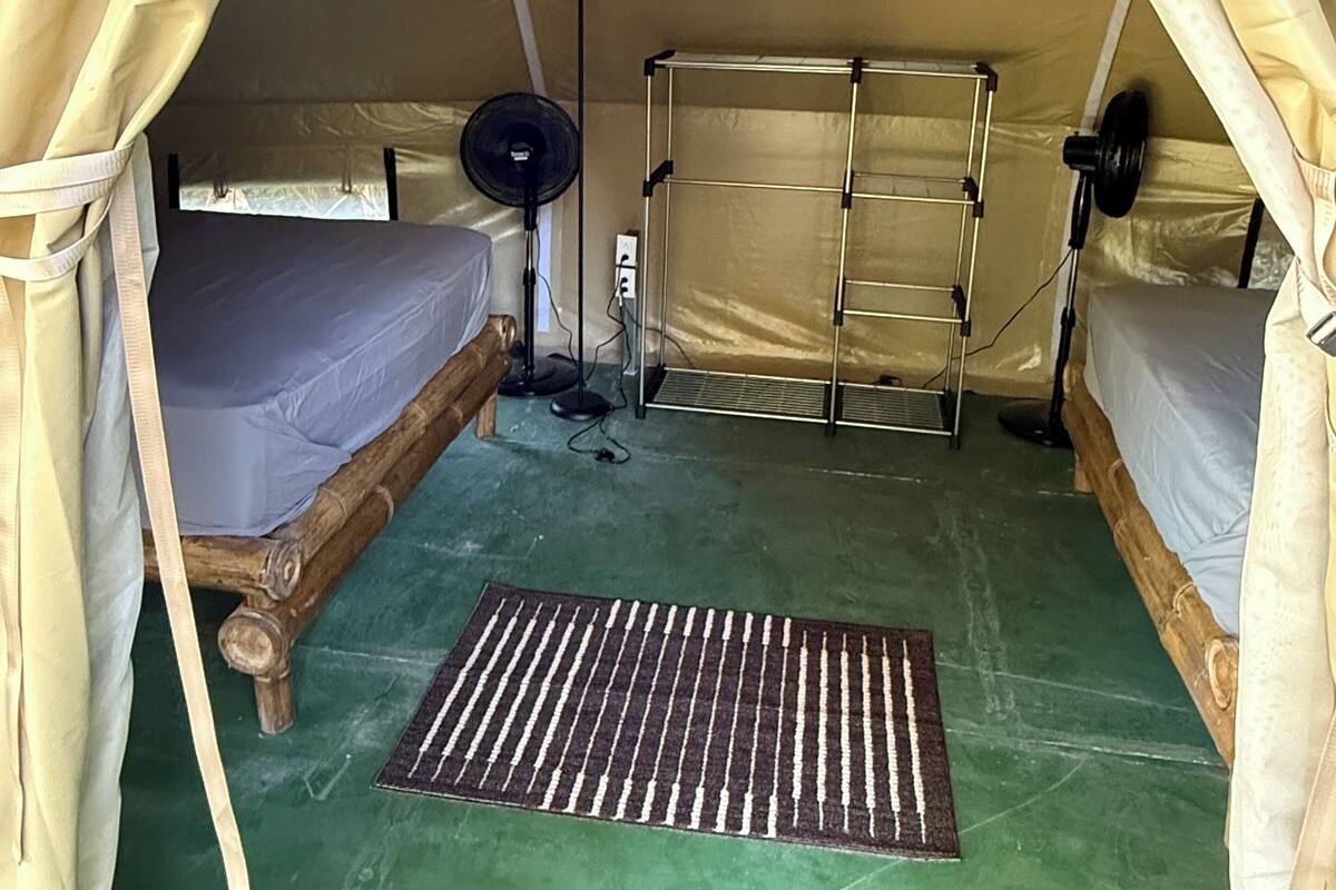 A tent with two beds, a floor lamp, and a power outlet.