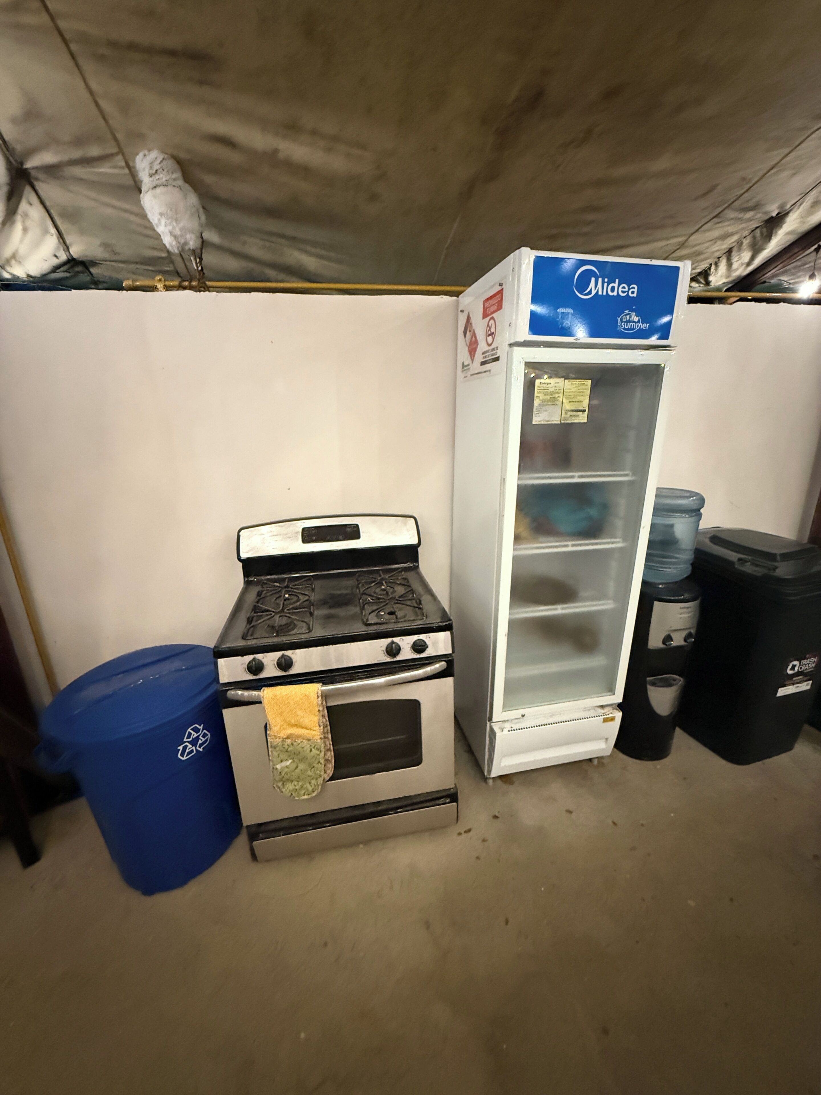 A kitchenette with a stove, a refrigerator, and a trash bin.