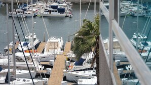 Un port de plaisance avec des bateaux amarrés, un palmier et des bâtiments en arrière-plan.