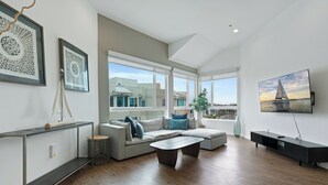 Un salon spacieux avec une grande fenêtre, un canapé, une table basse et un téléviseur posé sur un meuble.