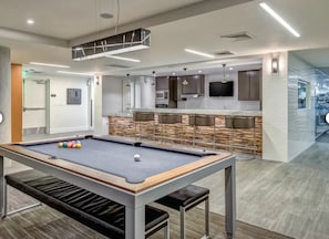 Une table de billard avec des billes, un coin bar et un téléviseur fixé au mur.