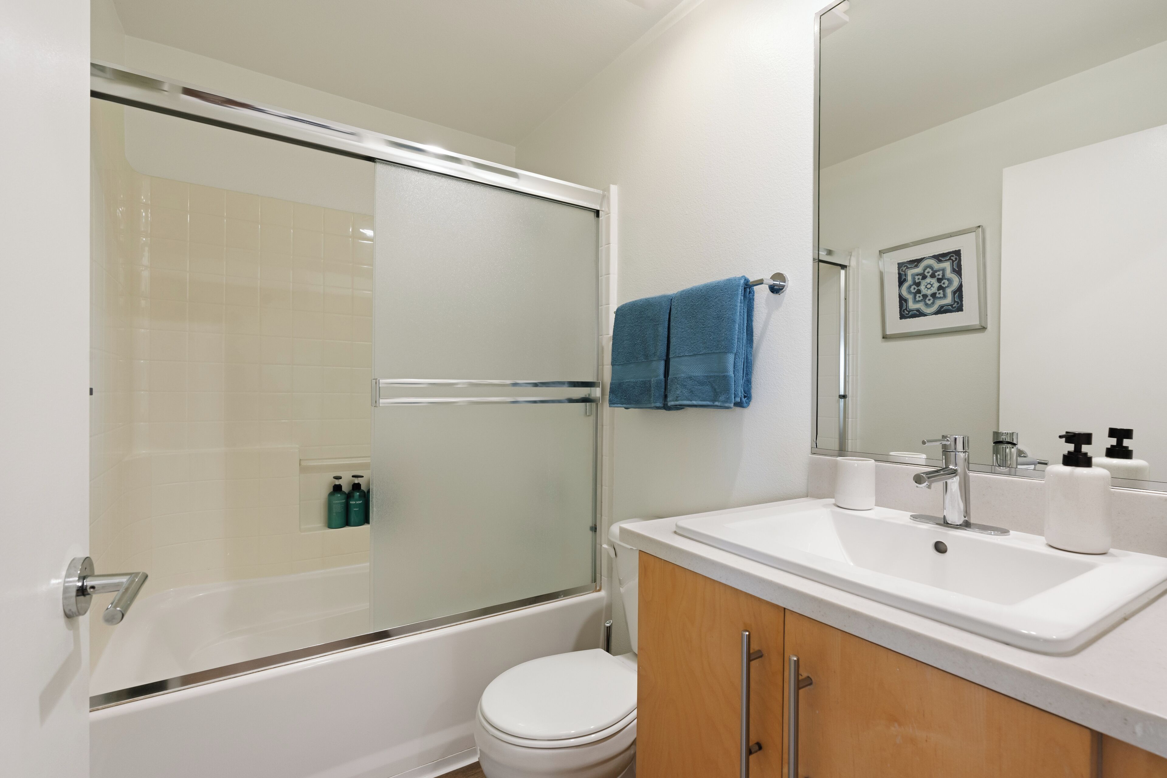 A modern bathroom with a glass-enclosed shower, a white toilet, a sink with soap dispensers, and a mirror above the sink.