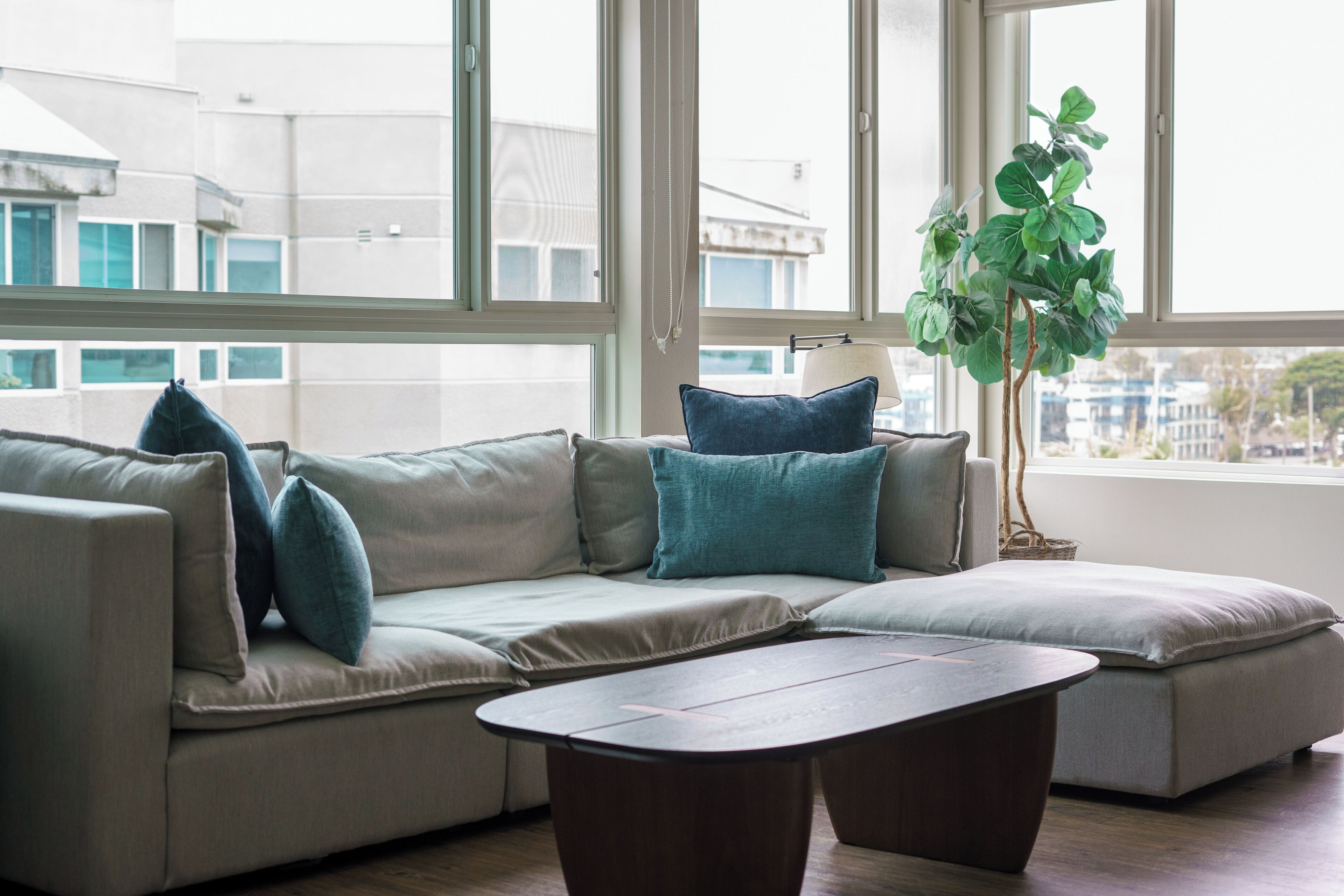 A modern living room with a sectional sofa, two side tables, and a large window with a view of buildings.