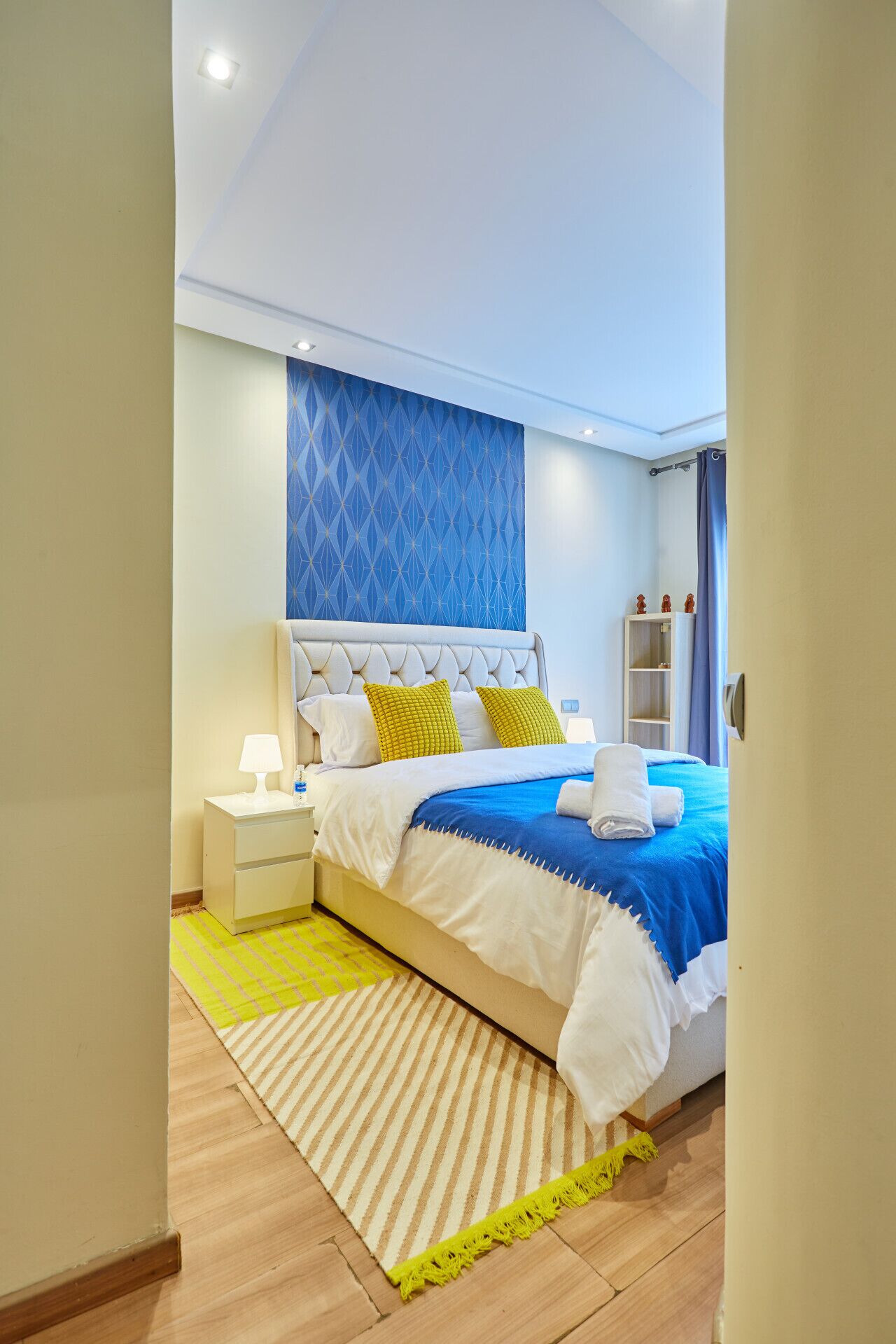 Ein modernes Schlafzimmer mit Bett, Nachttischen, einer Ablagefläche, einer blauen Wand mit Muster und Holzboden.