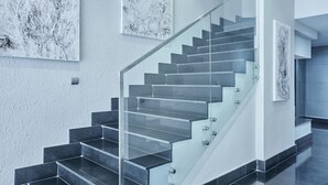 A modern staircase with glass railings, leading to a landing with a door.
