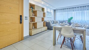 A modern living room with a dining area, built-in wooden shelving, and a grey sofa.