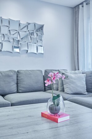 A modern living room with a grey sofa, a coffee table with a book and a glass dome plant, and a wall with abstract geometric decor. - Chic 3BR in Racine by Bd Massira (Casablanca)