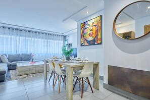 A modern living room with a dining area, a sofa, a coffee table, and a large painting on the wall. - Chic 3BR in Racine by Bd Massira (Casablanca)