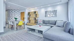 A modern living room with a grey sofa, a dining table with chairs, a coffee table, and built-in wooden shelving.
