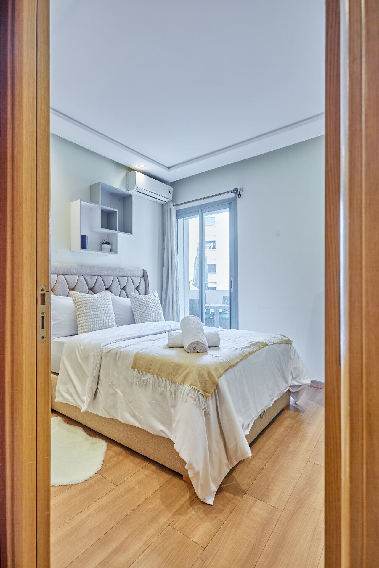 A bedroom with a bed, a bedside table, a window, and an air conditioning unit.