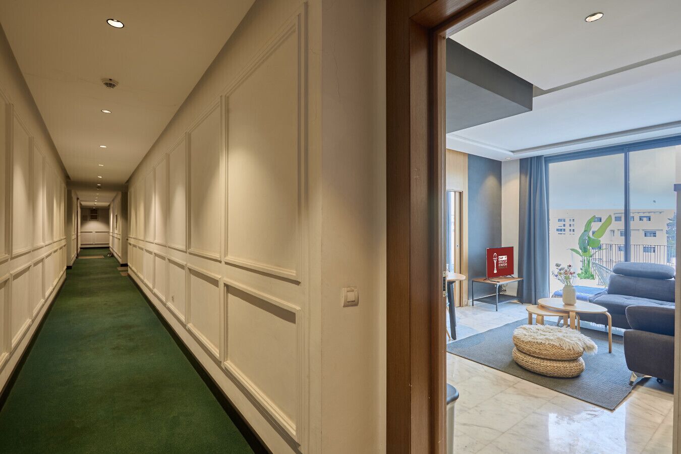 Ein Hotelgang mit grünem Teppich, einem großen Fenster und einer Sitzecke mit einer Couch und einem kleinen Tisch.