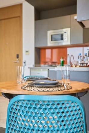 Una mesa de comedor con sillas azules, un microondas arriba y una cocina al fondo.