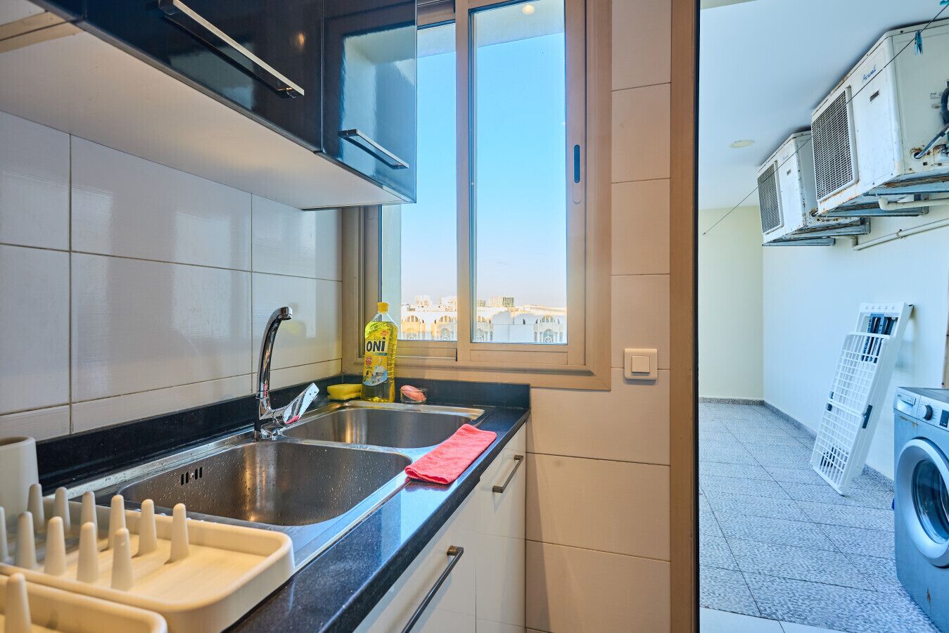 Eine moderne Küche mit Spüle, Geschirrgestell, einem Fenster mit Blick und einer Waschküche inklusive Waschmaschine und Trockner.