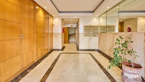 Un vestíbulo de hotel con suelo de mármol, taquillas de madera, una escalera y una planta en maceta.
